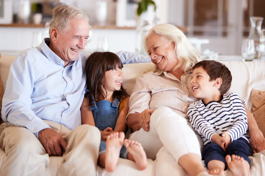 White senior couple and their grandchildren sitting on a sofa together smiling at each other