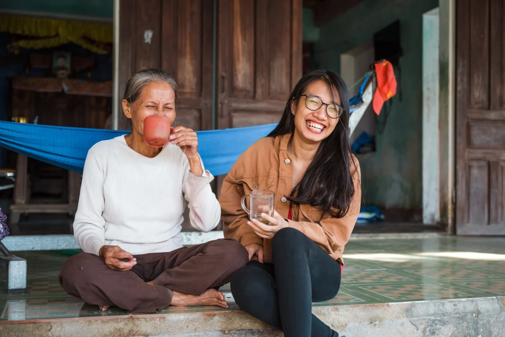 happy vietnamese senior woman sitting together with young woman on terrace and drinking tea