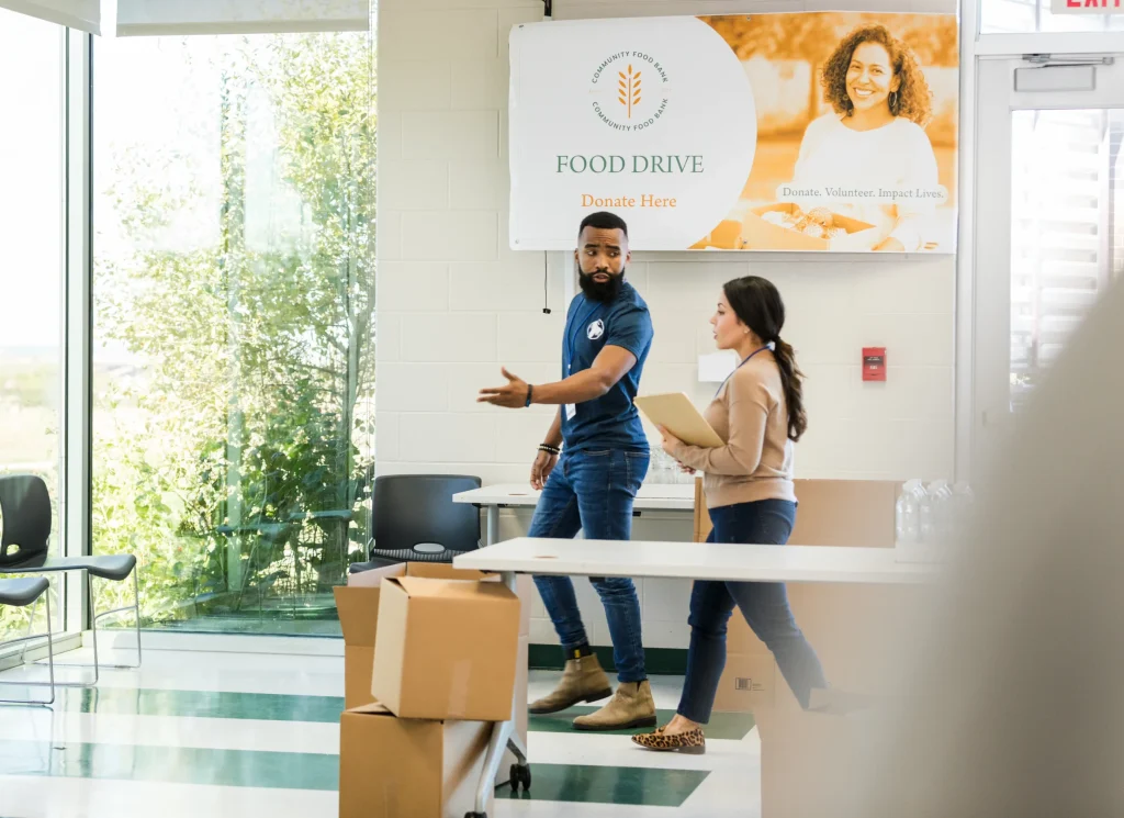 Two volunteers organize donations at a food drive. Teamwork and community support.