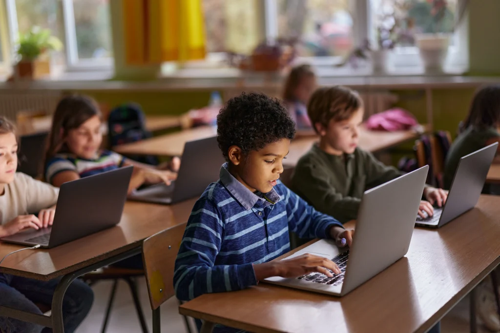 African American elementary student and his friends studying over computers during a class in the classroom.