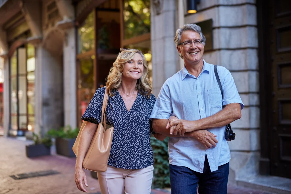 Elderly happy couple walking together in a city and smiling. Older man and beautiful senior healthy woman enjoying a relaxing city stroll. Happy old tourists exploring the town and spending time together arm in arm.